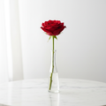 Single red rose in a slim glass bud vase on a marble table