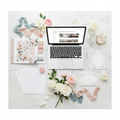Flat-lay of a wedding floral planning suite with mood boards, checklists, and a laptop on a marble surface