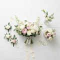 Flat-lay of wedding flower package with bridal bouquet, boutonnieres, and centerpieces on white linen