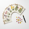 Six pressed-flower greeting cards fanned out on a pale desk