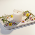 Botanical soy candle in frosted glass jar surrounded by wildflowers on a marble tray